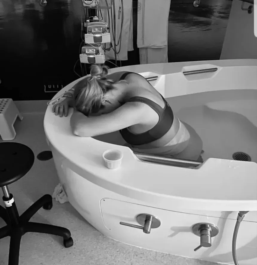 A woman in labour rests her arms on the rim of an AQVA maternity bath