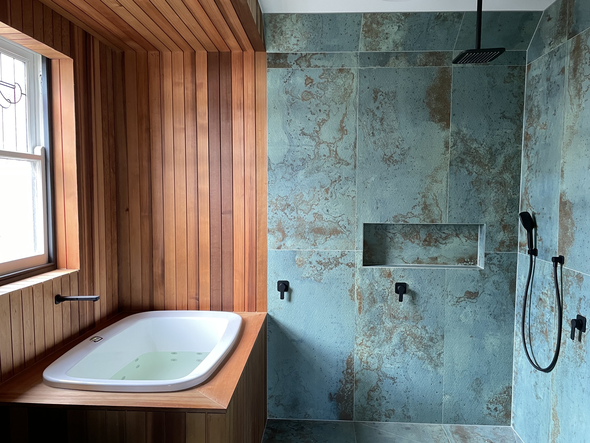 An insert bath in a timber surround in a timber-lined ensuite, with a tiled walk-in shower alongside